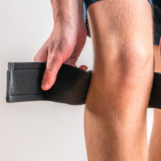 Orthoswiss Mini Kniebandage in Schwarz, Person zieht den Klettverschluss am seitlichen Gurt fest.