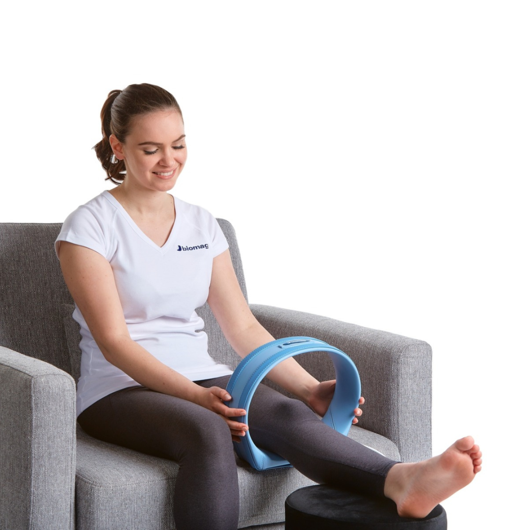 Person sitzt entspannt auf dem Boden und verwendet den ovalen blauen Biomag SL29 Sigma 2 Magnetfeldtherapie Applikator am Knie.