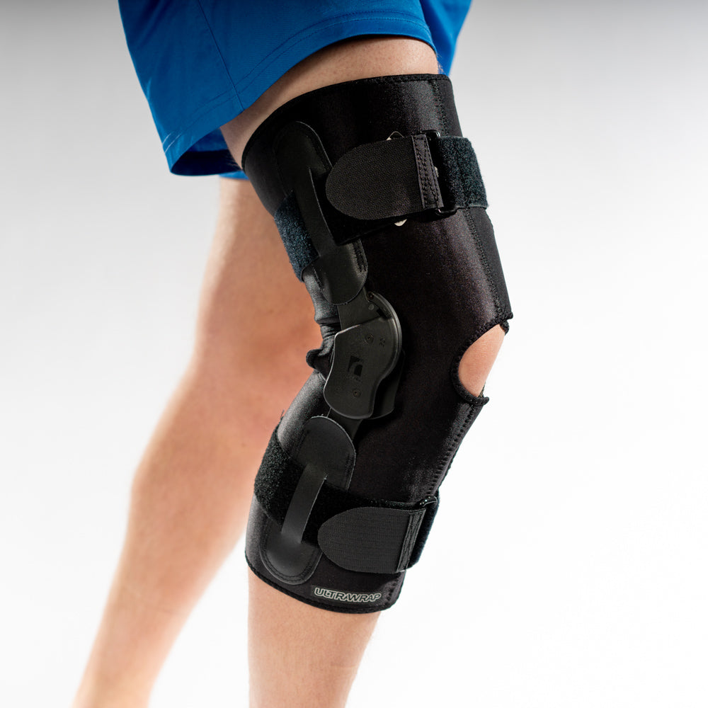 ULTRAWRAP Kniebandage am rechten Bein, Seitenansicht, schwarze Softbrace mit seitlichen Scharnieren und Öffnung vorne.