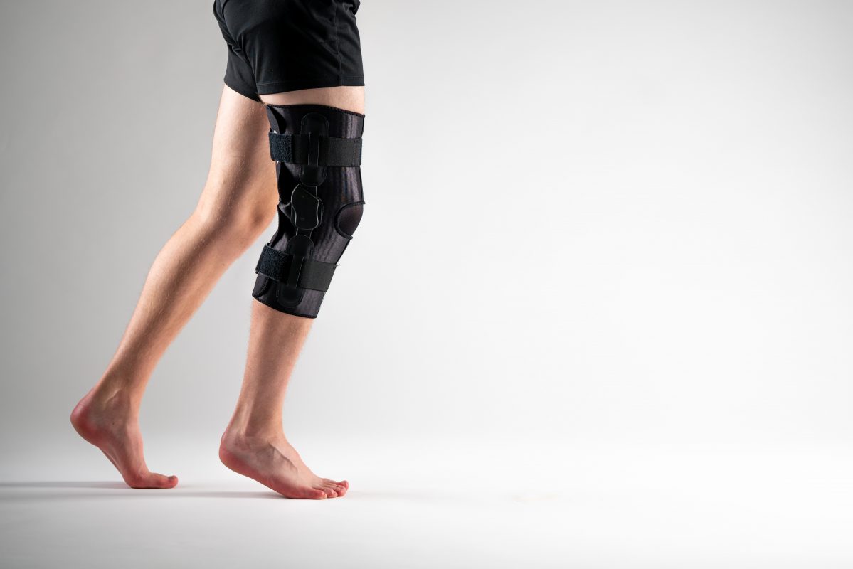 ULTRAWRAP Kniebandage am rechten Bein, Seitenansicht, schwarze Bandage mit Scharnieren und Klettverschlüssen. 