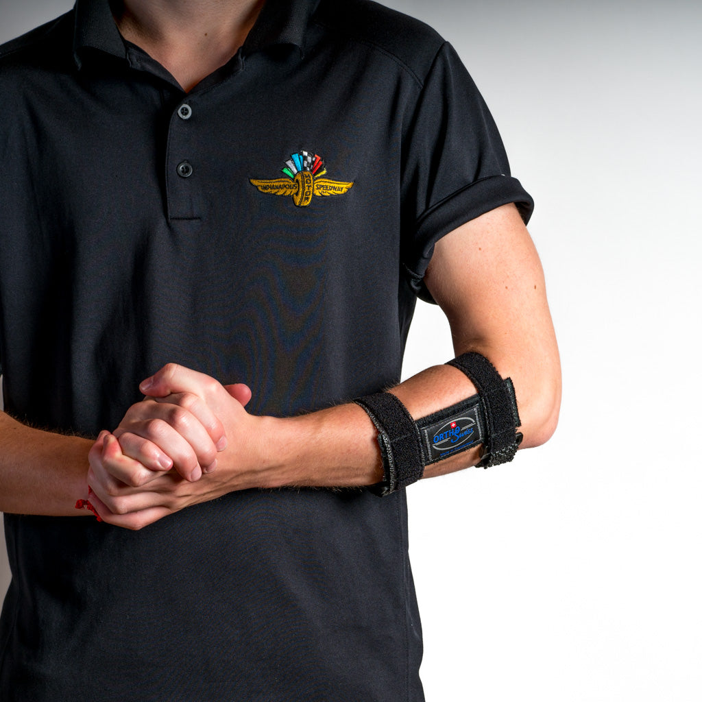 Schwarze OrthoSwiss EPI FIX Tennisarmbandage am Unterarm, frontal aufgenommen, Person verschränkt locker die Hände vor dem Körper.
