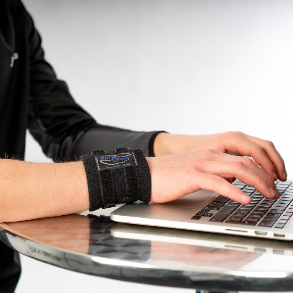 Hand mit OrthoSwiss Handgelenkbandage liegt auf Laptop, unterstützt bei Schmerzen und Entzündungen.