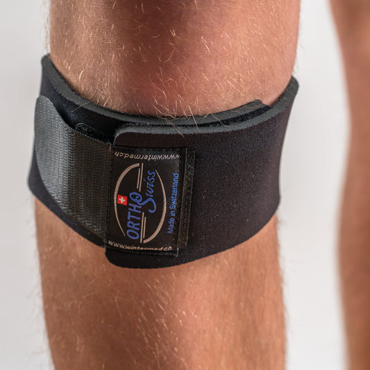 Orthoswiss Mini Kniebandage in Schwarz, Nahaufnahme von vorn, Logo und Klettverschluss klar sichtbar, unterhalb der Kniescheibe positioniert.